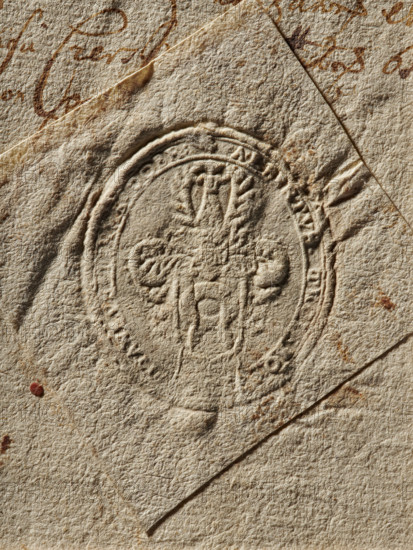 Oval dry impression of the seal of Wojciech Trojanowski, starost of the Dobrzyn Land. Nalecz coat of arms with a jewel above a crowned shield with labres. Partially illegible rim inscription: ALBERTUS TROIANO, CAPITANEUS TERRA DOBR, 1662. Poland; seal; dimensions 32.2 × 36 mm., A close-up of textured, aged paper in beige and tan tones with a pressed circular seal in the center; the seal creates raised and indented patterns and is surrounded by concentric rings. The paper shows a few folded edges and overlapping layers, with several small stains and spots in brown and reddish hues. There is visible rough fiber texture across the surface and some darker brown ink-like markings partially visible near the top edge.