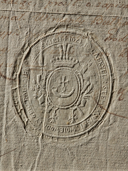 Seal of Józef Gabriel Stempkowski, Voivode of Kiev, Józef Gabriel Stempkowski (1785–1790). Oval dry impression of the seal. The Suchekomnaty coat of arms in an oval cartouche below a crown; beneath it the Order of the White Eagle and the Order of St. Stanislaw on ribbons. Inscription around the rim: IOZEF GABRYEL STEMPKOWSKI VOIVODE AND GENERAL OF THE KIEV LAND, 1786. Poland. Stamp. Sizes: 50.5 mm and 57.5 mm., The image shows a textured, beige paper surface with an embossed circular seal in the center; the seal has raised ornamental details including a central shield-like emblem topped by a crown and flanked by decorative foliage, with surrounding concentric circular bands and decorative elements around the lower edge. The paper surface displays visible creases, fibers, and slight tears, with scattered faint brownish ink marks and smudges across the background. The dominant colors visible are beige, tan, and brown with subtle variations in tone.