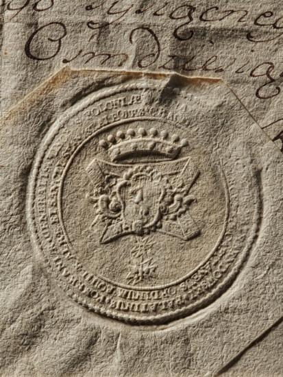Seal of Ignacy Franciszek Przebendowski, Starost of Kraków (Ignacy Franciszek Przebendowski, 1730–1791). Oval imprint showing in a decorative crowned cartouche the Kuna coat of arms; ribbons on the sides bearing the Order of the White Eagle. On the double rim a partially illegible inscription including 'PALATINUS POMERANIAE GENERALIS MINORIS POLONIAE' and titles such as 'CAPITANEUS. ORDINUM AQUILAE. ALBAE. ET SANCZ'. Dated 1782, Poland. Stamp; sizes: 55 mm and 58 mm., A close-up of textured paper showing an embossed circular seal with a detailed crest and decorative elements, placed on top of another sheet with cursive handwriting visible around the seal; the visible colors are beige, tan, brown, and dark brown.