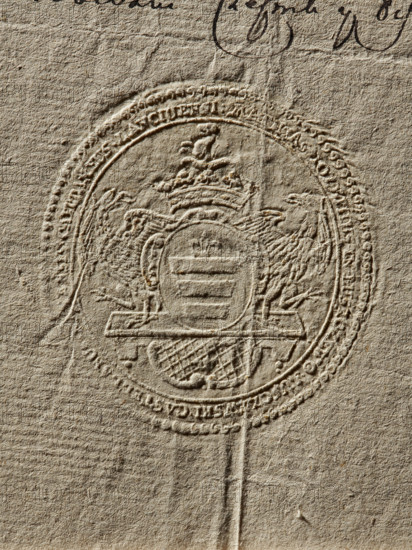 Seal of Maciej Luszczewski, Starost of Leczyca. Oval seal impression of the Starost of Leczyca, Castellan of Rawa and Sochaczew, Maciej Luszczewski. In a decorative cartouche on the console, the Korczak coat of arms with a jewel above a noble crown. The shield is supported by two eagles. The inscription on the rim is illegible. 1791, Poland. Seal; dimensions 1: 51 mm; dimensions 2: 53.5 mm., The image shows an embossed circular seal pressed into textured beige paper, creating raised and recessed patterns; the seal contains a central shield flanked by a pair of stylized birds and topped by a decorative crown-like emblem, with ornate edging and a few concentric rings around it; the paper surface displays visible fibers, small creases, and subtle shadows in tones of beige, tan, and light brown.