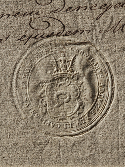 Seal of Sebastian Dluski, starost of Luków; round seal impression. On the decorative shield, the Nalecz coat of arms with a jewel above the rank crown. In the rim, the inscription: SEBASTIANUS ADLVGIE DLVSKI CAPITANEVS LVKOWIENSIS, 1783, Poland., A close-up view of textured paper in beige and tan tones, showing an embossed circular seal with ornate decorative elements including a crowned emblem and a central ornate shape, surrounded by a raised circular border; above the seal there is cursive handwriting in dark brown ink with flowing loops and strokes, and the paper surface shows visible fibers and creases with varied shadows and highlights.