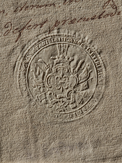 Seal of Jan Kicki of Kitki, Starost of Lviv. Round seal impression showing the Gozdawa coat of arms with a jewel above the rank crown placed in a cartouche decorated with panoplies; below, on a ribbon, the Order of the White Eagle. Around the rim, a partially illegible inscription: IOANNES IN KITKI KICKI, LEOPOL, ., 1770, Poland., A close-up of textured paper in beige and tan tones showing an embossed circular seal with decorative heraldic elements including a central stylized floral or fleur-like motif, ornate flourishes, and symmetrical ornamental shapes radiating outward; the embossed impression creates raised and recessed areas casting subtle shadows in brownish-beige, taupe, and cream hues, and there is a small area of darker reddish-brown handwriting partially visible near the top edge.