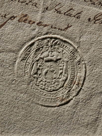 Seal of Antoni Barnaba Jablonowski, starost of Miedzyrzecz. Round impression of the seal in a decorative cartouche on a red field, showing the Prus coat of arms (Prus variety). In a double-headed bird interrupted by a two-headed eagle. Partially illegible inscription: 'ANTONIUS BARNAB, PALATINUS // POSNANIENSIS MEDE, CAPITANEUS.' Dated 1768, Poland. Seal/stamp., The image shows a close-up of textured paper in shades of beige and light brown with a circular embossed seal in the center featuring raised decorative elements and patterns; there is a group of flowing dark brown ink marks near the top edge, and subtle darker brown spots and smudges scattered around the paper surface.