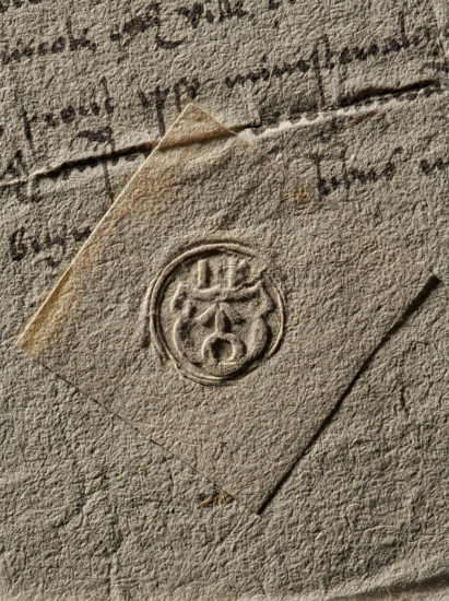 Seal of the Starost of Pyzdry (ca. 1563). Round impression of a seal: on the decorated shield, the Ogonczyk coat of arms; above the shield, the initial I.K.; dated 1563; Poland., A close-up of textured paper in beige and tan hues with a diagonal strip of slightly lighter paper overlaying it, featuring a circular embossed seal impression near the center; the surface shows a few dark brown ink marks and smudges, subtle creases and folds, and areas of shadow creating depth, with visible fibers and grain throughout in shades of beige, tan, brown, and off-white.