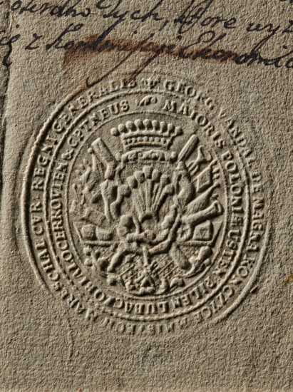 Seal of Jerzy Wandalin Mniszech, Starost General of Greater Poland; Jerzy August Wandalin (1715–1778). Oval impression of the seal: in a decorative cartouche the Mniszech coat of arms under a nine-baton crown. Behind the shield placed on a console are numerous panoplies; below it the Order of the White Eagle. In a double rim a partially illegible inscription: 'GEORG WANDAL DEMAGNA KONCZYCE, MARESCHAL CVR REGNI GENERALIS // MAIORIS POLONIAE USTEN PILEN LUBACZO BIALOCERKOVIEN & CAPTNEUS, 1768'. Stamp; dimensions 1: 55 mm, 2: 61 mm., A close-up of a textured beige paper with an embossed circular seal featuring ornate raised patterns including a crown-like motif and decorative elements radiating from the center, surrounded by a concentric raised border; above the seal there is dark brown handwritten ink with a darker brown horizontal stain, and the visible colors in the image are beige, light brown, dark brown, and hints of off-white in the highlights.