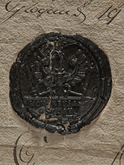 Seal of the Royal Prussia office in Glogów on documents, Zurakowski, Witold (?-1927) — official seals, seals on documents, seals with a coat of arms, two wax seals on one document with traces of a third. Wax impression of the seal of the Royal Prussia office in Glogów: crowned eagle with a sword and scepter in its talons, with a crown around its neck; inscription in the field: KON, PREUS AMT // GLOGAU. 1786, Glogów, Prussia, seal., A worn circular dark seal with a glossy surface is affixed to textured beige paper; the seal shows a raised double-headed bird motif with spread wings and ornate detailing, and the seal's edges and interior are cracked and chipped with small areas where the dark material is missing, revealing lighter paper beneath; there are a few strands of fiber crossing the seal and faint curved ink marks on the surrounding paper in dark brown.