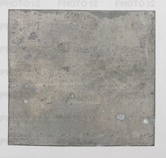 Sketch of a woman's head; Feliks Jablczynski (1865–1928), graphic artist; studies of women's heads; head studies; women; Polish graphics; Poland; ca. 1924; Warsaw; graphics; graphic matrix/plate; height 6.7 cm; width 7.4 cm, A square, flat surface fills most of the image, bordered by a narrow frame and set against a lighter background. The central surface shows a rough, worn texture with irregular patches and speckles, exhibiting mainly gray and muted beige tones, with several small pale bluish-gray spots and a few off-white specks. The surrounding border and outer area are a lighter gray, and the edges of the central square appear slightly darker than its interior. The overall appearance is of an aged, weathered material with subtle variations in tone and scattered blemishes.