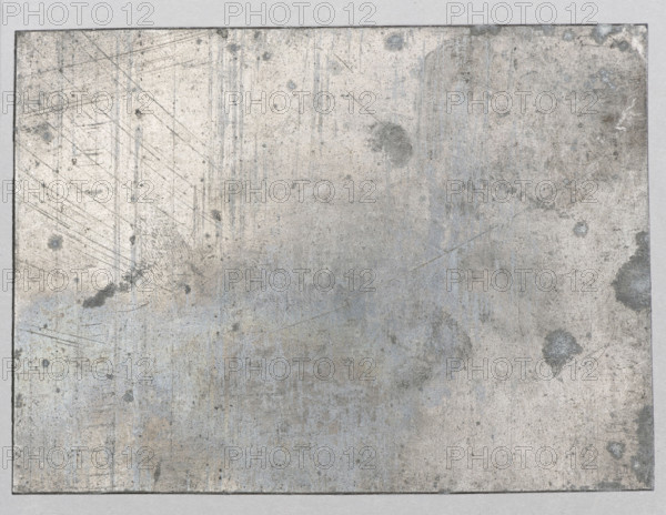 Buildings on a hill inspired by Polish architecture; Feliks Jablczynski (1865–1928), graphic artist; landscape and architectural study showing castles, towers, views, and gates; Polish graphics; ca. 1924, Warsaw; graphic matrix/plate; 7.4 cm x 10.2 cm., A rectangular, weathered metal sheet with a rough, mottled surface fills the image; the sheet shows a mix of gray, silver, light blue, and muted brown patches with darker gray spots and smudges scattered across it, as well as faint vertical and diagonal scratches and streaks in slightly darker gray; the metal has areas of subtle discoloration and faint rust-like tones, and the sheet sits against a pale gray background with a thin darker edge visible around the perimeter.
