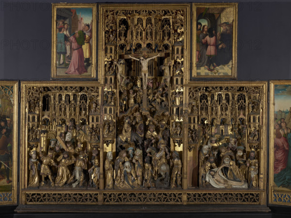 Crucifixion Polyptych from Pruszcz — middle part: carved wooden altarpiece panel depicting the Road to Golgotha with the Carrying of the Cross (left), the Crucifixion (center), and the Lamentation (right), framed by richly fragmented tracery canopies and small typologically paired scenes from the Old and New Testaments at the sides. The carved wardrobe is divided vertically into three zones in a standing-rectangle format, the central zone higher than the side ones (by 2/5 of the height). In the central zone three large Gothic windows appear in the background, and despite a landscape background with rocky ground and buildings the windows suggest the scene takes place in the church chancel. A strip of tracery decoration runs along the full width as a plinth. The sculptures are gilded except for painted faces and hands in flesh tones; background architecture and tracery are also gilded. ca. 1500, Antwerp; altar; height 242.0 cm, width 288.0 cm, thickness 41.3 cm., A large ornate wooden al...