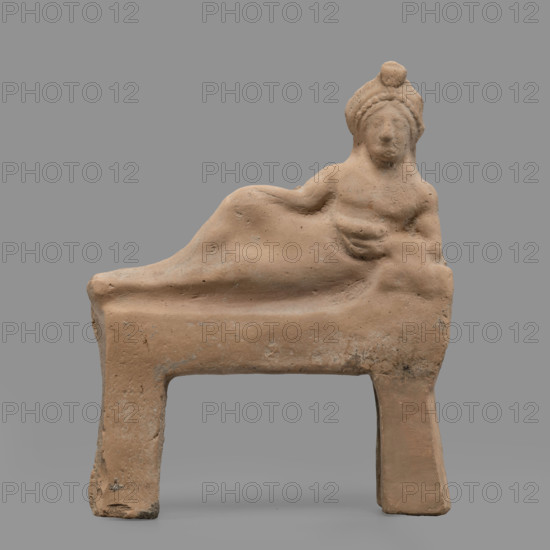 Figurine of a feasting Dionysus — figurine of a feasting man resting on a bed in a semi-reclining position, leaning on his left elbow and holding a cup in that hand. The torso is naked and the lower part of the figure is covered from the waist with a cloak, the end of which is thrown over the left forearm onto a pillow. On the head is a diadem decorated with pearls, an astral rosette above which a lotus flower protrudes. Red clay, medium-grained with tiny mica particles. 5th century BC (dating before the 2019 revision: late 6th century BC; analogous artifact dated to 480–470 BC), Tarentum. Figurine, height 19 cm, width 15.2 cm, depth 3.3 cm, weight 0.34 kg.