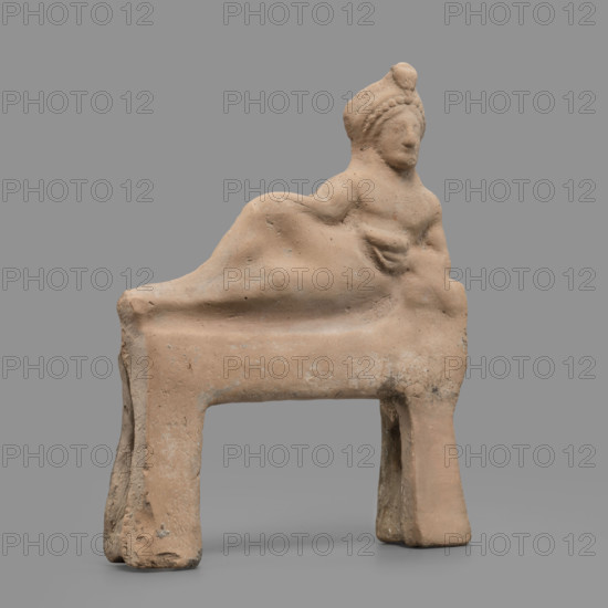 Figurine of a feasting Dionysus, author Scen.Gal.Klass. Figurine of a feasting man resting on a bed in a semi-reclining position, leaning on his left elbow and holding a cup in that hand. The torso is naked and the lower part of the figure is covered from the waist with a cloak, the end of which is thrown over the left forearm onto a pillow. On the head is a diadem decorated with pearls, an astral rosette above which a lotus flower protrudes. Red clay, medium-grained with tiny mica particles. 5th century BC (dating before the 2019 revision: late 6th century BC; analogous artifact dated to 480–470 BC). Tarentum, figurine. Height 19 cm, width 15.2 cm, depth 3.3 cm, weight 0.34 kg.