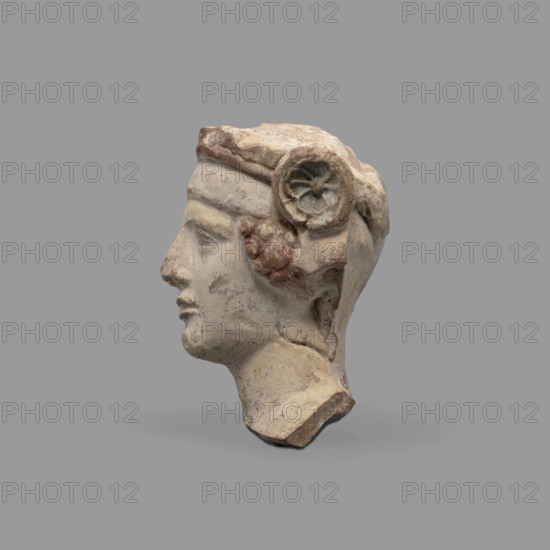 Head of a figurine of Dionysus. Head of a young man with a face devoid of [expression], wide compact mouth, triangularly outlined face with carved cheeks, large eyes, prominent nose and gently outlined eyebrows. The youth wears a diadem decorated with rosettes at the sides and a thick wreath. Traces of red paint (cinnabar) on the hair, lips and diadem; blue in the rosette recesses and on the wreath. 5th–4th century BC, Taranto, Southern Italy, figurine. Height 8.7 cm, width 8.3 cm, depth 6.3 cm, weight 0.28 kg.