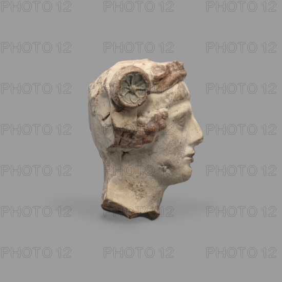 Head of a figurine of Dionysus. Head of a young man with a face devoid of expression, with a wide, compact mouth, a triangularly outlined face with carved cheeks, large eyes, a prominent nose and gently outlined eyebrows. On his head the youth wears a diadem decorated with rosettes on the sides and a thick wreath. Traces of red paint (cinnabar) on the hair, lips and diadem. Blue on the rosettes — in the recesses. 5th–4th century BC, Taranto, Southern Italy (Italy). Terracotta figurine, height 8.7 cm, width 8.3 cm, depth 6.3 cm, weight 0.28 kg. Author: Scen. Gal. Class.; inscription/revindicaton noted.