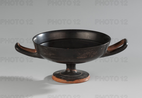 Black-finned kylix, Vicup type. Vicup type kylixes are characterized by a straight edge and a concave outer wall of the foot, which has a reserved surface. The lower surface of the foot is concave, decorated with a wide band of black varnish. The vessel has two handles mounted at the level of the rim. Technology: entire surface covered with an evenly distributed, glossy black varnish of good quality. Traces of turning visible under the varnish. Clay is cleaned. Comments: surface dirty, with visible chips, scratches, and abrasions. Fragment of the foot is glued on. Visible conservation additions. Clay color: 2.5 YR 6/6 (light red). Varnish color: 10 YR 2/1 (black). Ca. 480 BC (ML Bernhard dates the monument to ca. 480 BC). Attica. Vessel: kylix. Height 7.6 cm; width 20.7 cm; depth 14.2 cm; weight 0.210 kg.