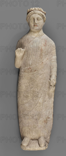 Votive figure of a youth holding a bird, votive offerings, Cypriot sculpture. Figurine of a youth shown standing; left arm down at his side with a 'handkerchief' visible in his hand, right arm bent at the elbow and raised upwards, palm open and frontal. Dressed in a chiton and himation; folds of the chiton marked with slightly wavy shallow lines, folds of the himation highlighted with an engraved schematic line. Head relatively small with regular features, visible eyes, straight nose, and traces of red polychrome on the lips. Hairstyle of small curled locks arranged in two rows; hair decorated with a diadem with traces of red polychrome. Back of the sculpture unfinished. Date: 480–310 BC (previous dating: first half of the 5th century BC). Cyprus. Sculpture. Height 43 cm, width 14 cm, depth 14 cm, weight 3.03 kg.