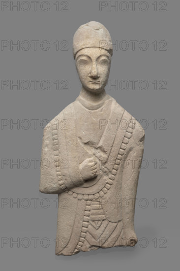 Fragment of a votive figure of a man. The fragment depicts a standing man dressed in a tutulus and himation. The outer edge of the himation is framed by an ornament in the form of semicircular serrated edges. The torso is flattened, the front part is carefully detailed, while the back is flat. The right arm, bent at the elbow, rests on the chest. The right hand is lowered down, close to the torso, the hand clenched into a fist. The face is oval, elongated. The chin is small, the lips are thin, and the nose is long and aquiline. The eyes are slanted and prominent, the eyebrows are arched, and the forehead is low. Conical headdress. Proto-Cypriot Style II, circa 600–480 BC. Cyprus; sculpture. Height 28 cm, width 14 cm.