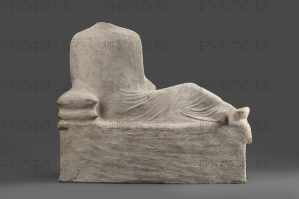 Depiction of a deceased person on a keline and a servant; banquet scene, Cypriot sculpture. The sculpture depicts a man banqueting in a semi-reclining position on a keline (bed). His upright torso is supported by his left elbow placed on two pillows. The man is dressed in a long, finely pleated chiton and himation. In front of the bed, at the side of the banqueter's legs, stands a small boy dressed in a chiton on a cuboid base. 4th century BC (dating before the 2019 revision: 450–375 BC; Cypriot-Classical Period). Marion. Sculpture. Height 45 cm, width 53 cm, depth 24 cm, weight 13.03 kg.