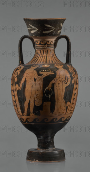 Red-figure amphora, Apulian workshop, repossession; Classical Period; 3rd quarter of the 4th century BC; Apulia (Italy). Amphora with a wide, tapering foot supporting a cylindrical stem, merging into a belly with short horizontal handles that arch into a narrow neck topped by a tall, diagonally widening spout covered with floral ornamentation. Neck decorated at the top with a wavy ornament; lower section ingot-shaped. Two ribbon-like handles run from the shoulders to the lower edge of the rim. Both sides of the body bear painted figurative scenes. Side A: a man and a woman standing opposite each other with an altar between them; the naked man holds a bowl in his outstretched left hand, a cloak slung over his arm, weight on his left leg; the woman wears a long chiton fastened at the shoulders and tied at the waist. Side B: two young men facing each other wearing cloaks; the young man on the right leans on a long stick with his right arm outstretched. Beneath the handles are large palmet...
