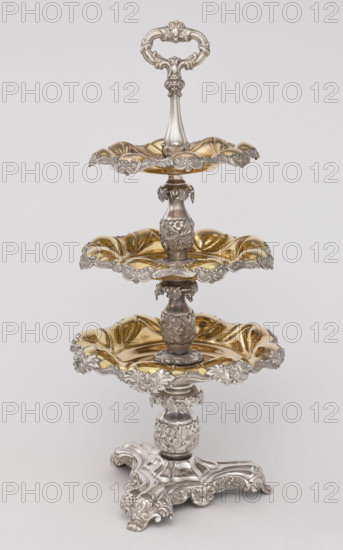 Etazera, Fraget, Józef (Warsaw; silver and plated goods factory; 1824–1945), tableware elements. Etazera — three-tiered platter on a three-sided base, with three knobbed plates, plated with gold on the outside and silver on the bottom, with silver-plated tin overlays on the edges. Finished with an oval decorative handle. Composed of two parts: the base and a plate holder inserted into a cylindrical opening. Marked with an oval Fraget mark with the date 1843. Vessel, 1843, Poland, Warsaw; height 57 cm, width 25.9 cm.