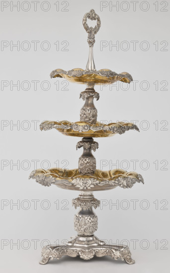 Etazera by Józef Fraget (Warsaw; silver and plated goods factory; 1824–1945). Three-tiered platter on a three-sided base with three knobbed plates, plated with gold on the outside and silver on the bottom, with silver-plated tin overlays on the edges. Finished with an oval decorative handle. Composed of two parts: the base and a plate holder inserted into a cylindrical opening. Marked with an oval Fraget mark dated 1843. Vessel, 1843, Poland, Warsaw. Dimensions: height 57 cm, width 25.9 cm.