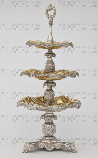 Etazera, Fraget, Józef; tableware elements. Etazera — three-tiered platter on a three-sided base, with three knobbed plates; plated with gold on the outside and silver on the bottom, with silver-plated tin overlays on the edges. Finished with an oval decorative handle. Composed of two parts: the base and a plate holder inserted into a cylindrical opening. Marked with an oval Fraget mark with the date 1843. Vessel, 1843, Poland, Warsaw. Dimensions: height 57 cm, width 25.9 cm.