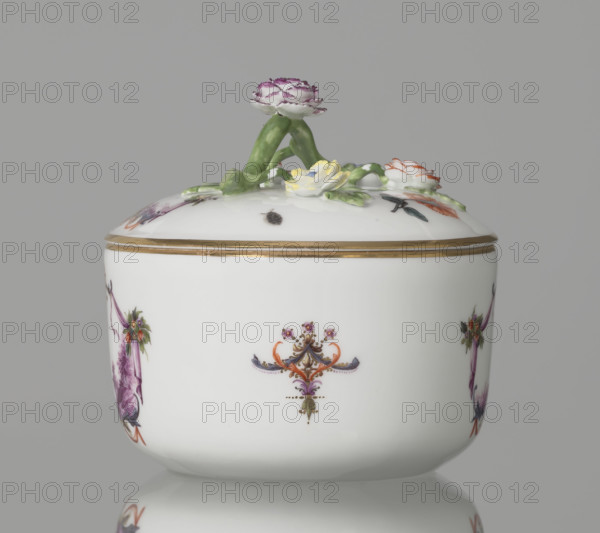 Sugar bowl with a lid and a branch handle, Koenigliche Porzellain Fabrique, Meissen (1710–1763), manufacturer; ca. 1750. Cylindrical sugar bowl, rounded at the base, with a slightly arched lid with a plastic, colorfully painted branch handle terminating in four flowers and leaves: three forget-me-nots, two brick-red flowers and one yellow. On the sides of the body two cartouche frames and on the cover one, each framed by purple draperies suspended from small flower bouquets and dry rocailles, topped and bottomed symmetrically with brick-red draperies suspended from plant branches. Within the cartouches are purple-camaieu landscape miniatures with architecture and staffage: (1) fragment of a hill with trees, two figures, and a building in a valley; (2) two buildings among bushes; cover: (3) a plateau with a house and a distant hill to the right. Between the cartouches on the body are two colorful ornamental-floral motifs; on the lid two woodcut flowers and three insects. Rim of bowl and...