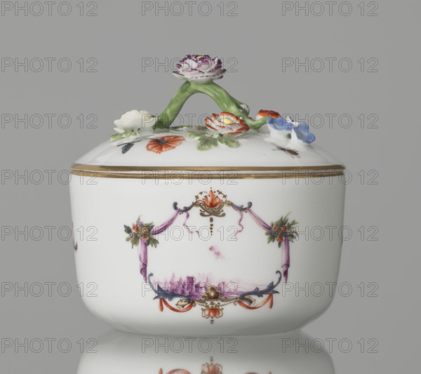 Sugar bowl with a lid and a branch handle. Koenigliche Porzellain Fabrique, Meissen (1710–1763), manufacturer. Porcelain sugar bowl, cylindrical, rounded at the base, with a slightly arched lid. Lid handle is a modeled, polychrome branch with four flowers and leaves at the ends of side shoots: three forget-me-nots, two brick-red flowers, and one yellow. On the sides of the body are two cartouche frames and one on the cover, each formed by purple draperies suspended from small flower bouquets and dry rocailles, topped and bottomed on the symmetry axis with brick-red draperies suspended on plant branches. Within the cartouches are landscape miniatures with architecture and staffage painted in purple camaieu: (1) fragment of a hill with trees, two figures, and a building in a valley; (2) two buildings among bushes; cover: (3) a plateau with a house and a hill in the distance at right. Between the cartouches on the body are two colorful ornamental-floral motifs; on the lid are two woodcut ...