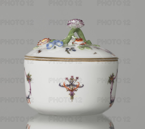 Sugar bowl with a lid and a branch handle, Koenigliche Porzellain Fabrique, Meissen (1710–1763), manufacturer. Cylindrical sugar bowl, rounded at the base, with a slightly arched lid topped by a plastic, colorfully painted branch handle with four flowers and leaves at the end of the side shoots: three forget-me-nots, two brick-red flowers and one yellow. On the sides of the body two cartouche frames and on the cover one, each with two purple draperies suspended from the sides on small flower bouquets and dry rocailles, topped and bottomed on the axis of symmetry with brick-red draperies suspended on plant branches. Within the cartouches are landscape miniatures with architecture and staffage painted in purple camaïeu: (1) a fragment of a hill with trees, two figures, and a building in a valley; (2) two buildings among bushes; (3, on the cover) a plateau with a house and a hill in the distance on the right. Between the cartouches on the body are two colorful ornamental-floral motifs; on...