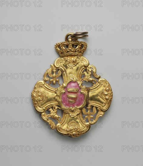 The Grand Cross of the Order of the Polish Canonesses of Warsaw, an equal-armed cross with a grand Baroque form, the arms forming the axes of a four-field coat of arms of the Republic of Poland. The spaces between the arms, enclosed by arabesque connectors, form fields containing openwork coats of arms of the Crown and Lithuania, the Eagle, and the Tail alternately placed heraldically. At the intersection of the arms on the obverse is a movable shield-shaped plaque with the Korczak coat of arms on an amaranth enamel background; it is hinged on the right and has two small holes for pegs. The reverse of the plaque retains remnants of enamel. Beneath the plaque is an oval reliquary containing remains of St. Adelaide. On the reverse at the intersection is a plaque showing Our Lady of the Immaculate Conception on a blue background. The cross is topped with an openwork crown bearing a suspension ring. Dated 1744, Poland.