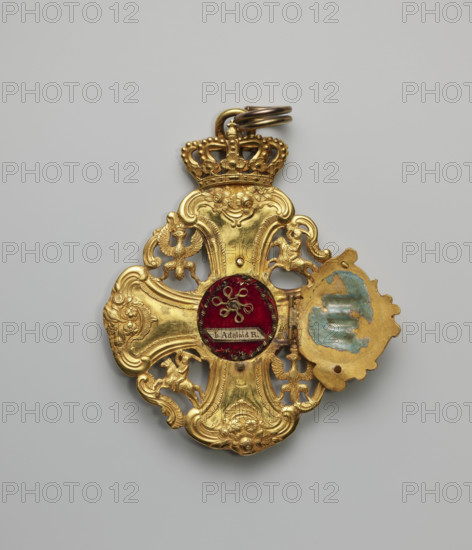 The Grand Cross of the Order of the Polish Canonesses of Warsaw, an equal-armed cross with a grand baroque artistic form, the arms forming the axes of a four-field coat of arms of the Republic of Poland. The spaces between the arms, enclosed by arabesque connectors, form fields containing openwork coats of arms of the Crown and Lithuania, the Eagle, and the Tail alternately placed heraldically. At the center on the obverse is a movable, hinged shield-shaped plaque with the Korczak coat of arms on an amaranth enamel background; the plaque has two small holes at top and bottom for pegs and the reverse of the plaque contains remnants of enamel. Beneath the plaque is an oval reliquary containing remains of St. Adelaide. On the reverse at the intersection of the arms is a plaque with the image of Our Lady of the Immaculate Conception on a blue background. The cross is topped with an openwork crown with a suspension ring. Dated 1744, Poland.