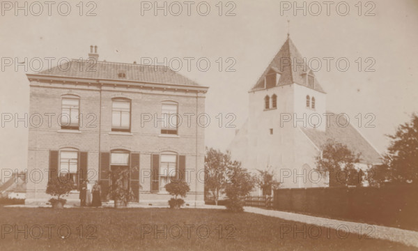 View of the Old St. Victor Church in Batenburg, photograph, page, photographer: Benjamin Charlé (possibly), Batenburg, c. 1903 - in or before 1908, paper, baryta paper, daylight collodion silver print, height 101 mm x width 163 mm, Photo on eighth unnumbered page., church (exterior), Oude Sint-Victorkerk, A sepia-toned photograph showing two adjacent buildings set behind a lawn. On the left is a two-story brick house with a tiled roof, rectangular windows with shutters on the ground floor and arch-topped windows on the upper floor, and a small group of people standing near the entrance beside potted plants and trimmed bushes. On the right is a pale stuccoed building with a steep tiled roof and a square tower topped by a pointed roof, featuring paired arched openings on the tower and a small gated area in front, with trees and shrubs partially obscuring the lower walls.