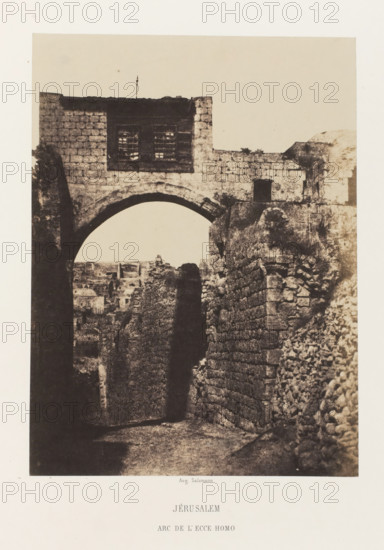Arch of Ecce Homo, Jerusalem, Jérusalem. Arc de l'Ecce Homo, photograph, page, photographer: Auguste Salzmann, printer (person): Louis-Désiré Blanquart-Evrard, Lille, publisher: Gide et J. Baudry, Paris, 1854 - 1856, Auguste Salzmann, Louis-Désiré Blanquart-Evrard, Gide et J. Baudry, photographer, printer (person), publisher, pasteboard, paper, salted paper print, height 212 mm x width 157 mm, Photo on unnumbered page., gate, entrance, A sepia-toned photograph shows a stone archway set within thick, weathered masonry, with a rectangular upper section featuring a barred window and textured stone blocks; a narrow, shadowed passage runs beneath the arch between rough stone walls that lead toward a distant cluster of low buildings visible through the opening, while rubble and uneven stones line the right side and the ground appears worn and uneven.