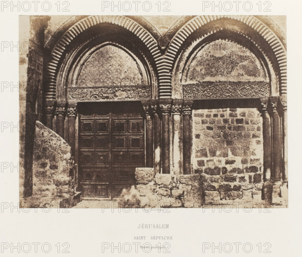 Main portal of the Church of the Holy Sepulcher, Jerusalem, Jérusalem. Saint Sepulcre. Entrée principale, photograph, page, photographer: Auguste Salzmann, printer (person): Louis-Désiré Blanquart-Evrard, Lille, publisher: Gide et J. Baudry, Paris, 1854 - 1856, printer (person), pasteboard, paper, salted paper print, height 153 mm x width 214 mm, Photo on unnumbered page., by, parts of church exterior and annexes: portal, Church of the Holy Sepulchre, A cropped sepia photograph of a stone building façade showing two rounded archways with striped voussoirs and decorative carved bands above them, one arch framing a textured surface and the other framing a patterned surface, beneath which stand columns with carved capitals and a large paneled wooden door; the lower area shows rough stone blocks, worn steps, and a low stone wall or balustrade in front of the entrance.