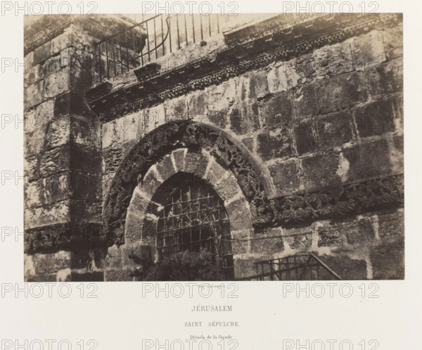 Jerusalem. Saint Sepulcre. Détails de la façade, Detail of a window of the Church of the Holy Sepulcher, Jerusalem, photograph, page, photographer: Auguste Salzmann, printer (person): Louis-Désiré Blanquart-Evrard, Lille, publisher: Gide et J. Baudry, Paris, 1854 - 1856, printer (person), pasteboard, paper, salted paper print, height 157 mm x width 224 mm, Photo on unnumbered page., window, parts of church exterior and annexes: facade, Church of the Holy Sepulchre, A close view of a stone facade showing a rounded archway with carved decorative patterns around the arch and a metal grille across the opening, rough textured masonry blocks forming the surrounding wall, a horizontal band of carved ornament above the arch, traces of weathering and discoloration on the stones, and a metal railing visible at the top and lower right edge of the image.