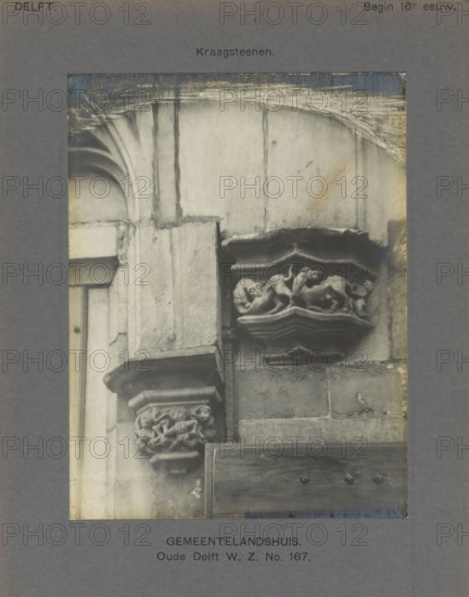 Corrugated stones of the Gemeenlandshuis on the Oude Delft in Delft decorated with fantasy creatures and humans, Gemeentelandshuis. Oude Delft WZ No. 167. Corrugated stones, photograph, inscription: 'Delft. Early 16th century.', inscription: 'The right of reproduction of these photos is reserved by the Publisher.', number: '23', number: '17', Delft, c. 1900 - c. 1904, photographer, paper, pasteboard, gelatin silver print, gelatin silver developing print, height 155 mm x width 118 mm, ornament, hybrid animals, Gemeenlandshuis, A close-up photograph of a stone architectural detail showing a corner of a building with carved corbels and capitals, featuring a rounded arch above and weathered stone surfaces; one corbel has a decorative relief with intertwined figures or animals, while another lower capital shows carved human heads; a wooden panel with visible bolts is set against the stone below, and the image is mounted on a gray mat with some wear and discoloration around the edges.