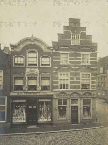 View of two houses and shops on the Wijnhaven in Delft, Wijnhaven No. 15 and No. 16, photograph, inscription: 'Delft. A No. 15. Louis XIV. B No. 16. Early 16th century', number: '24', inscription: 'The right of reproduction of these photos is reserved by the Publisher.', Delft, c. 1900 - c. 1904, photographer, paper, pasteboard, gelatin silver print, gelatin silver developing print, height 155 mm x width 115 mm, shop-window, show-window, A faded photograph shows two adjacent narrow brick buildings with ornate facades facing a cobbled street, the left building featuring a curved decorative gable and three tall windows on the upper floor above a shopfront with display windows and a central door, the right building displaying a stepped gable with horizontal light bands, multiple rectangular windows with small panes, and an arched decorative row above the upper shop windows, while a glimpse of another building and a sloped street appears to the right and a plain frame surrounds the image.