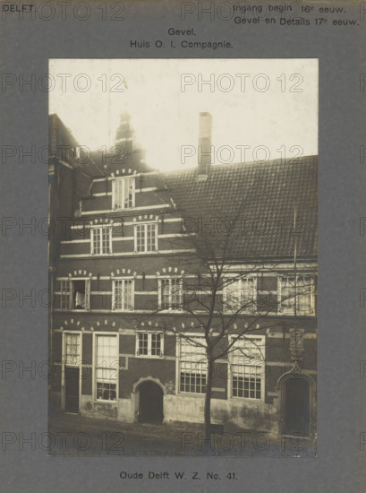 View of the East India House on the Oude Delft in Delft, Oude Delft WZ No. 41. Facade. House OI Company, photograph, number: '38', inscription: 'Delft. Entrance early 16th century. Facade and Details 17th century.', inscription: 'The right of reproduction of these photos is reserved by the Publisher.', Delft, c. 1900 - c. 1904, photographer, paper, pasteboard, gelatin silver print, developed gelatin silver print, height 170 mm x width 115 mm, urban housing, chimney, Oude Delft, A faded photograph of a multi-story brick building with decorative lighter trim around windows and along horizontal bands, a tiled sloping roof with a chimney, and stepped gables; several rectangular windows with small panes are visible, one window on an upper floor is open with a hanging cloth; an arched doorway at street level and a smaller ornate doorway with decorative surround are visible; bare tree branches partially obscure the facade and extend upward in front of the building; the image is mounted on a d...