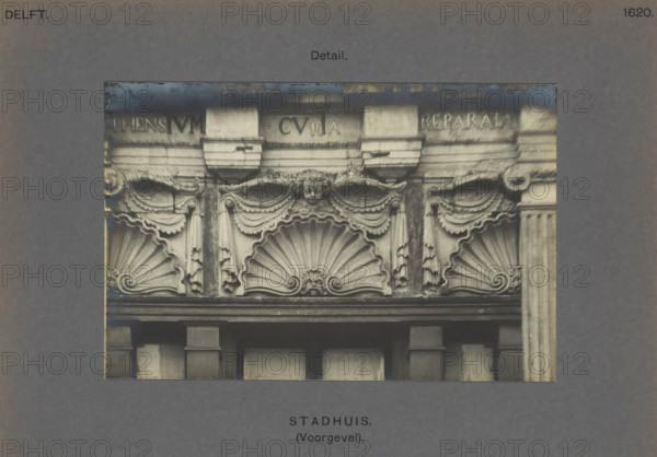 Town Hall (Facade). Detail, Detail of the façade of the town hall in Delft, decorated with shells and cherubs, photograph, inscription: 'Delft. 1620.', number: '48', inscription: 'The right of reproduction of these photos is reserved by the Publisher.', Delft, c. 1900 - c. 1904, photographer, paper, pasteboard, gelatin silver print, height 97 mm x width 148 mm, townhall, cherubs, i.e. children's heads with wings, scallop, shell, ornament - AA - stylized, Town Hall (Delft), A rectangular photograph shows a detailed stone facade with decorative sculpted elements including three large scallop shell motifs, draped garlands, and carved pilasters; a small carved face is centered above the middle shell, flanked by ornate scrolls and hanging tassel-like decorations; the stone appears weathered with darker staining in places and a horizontal cornice runs above the decorative band; the photo is mounted on a gray board with a wide border surrounding it.