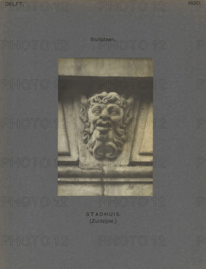Town Hall (South side.) Keystone, Keystone of the town hall in Delft, decorated with a head of presumably a faun, photograph, inscription: 'The right of reproduction of these photos is reserved by the Publisher.', inscription: 'Delft. 1620', number: '57', Delft, c. 1900 - c. 1904, photographer, paper, pasteboard, gelatin silver print, height 108 mm x width 75 mm, townhall, satyrs, fauns, Sileni, keystone, architecture, Town Hall (Delft), A central rectangular photograph shows a carved stone grotesque with a stylized face featuring curled hair, prominent ears, wide eyes, an open mouth, and a curled beard set within architectural stonework; the photograph is mounted on a dark textured background with small printed labels above and below the image.