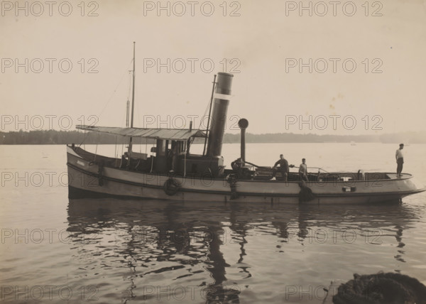 Tugboat Johanna, Ocean Harbor Belawan, photograph, The tugboat 'Johanna'. Numbered: 200. Part of the group of individual photographs regarding the construction of the harbor of Belawan on the coast off Medan, Sumatra 1921-1922., date: '11, 9-22', inscription: 'No. 200 Sleepboot Johanna', Belawan, 1922-09-11, photographer, Sumatra, paper, gelatin silver print, developing gelatin silver print, height 160 mm x width 220 mm, harbor, building-site, tug, pusher tug, economic history, overseas history, traffic and transport, infrastructure, dredging, Period, 1921 - 1922, A small steam-powered boat floats on calm water with its reflection visible below, showing a rounded hull with dark trim and mounted tires along the side, a cabin with a corrugated roof and open sides, a tall smokestack rising near the center, a vertical mast toward the rear, and various ropes and rigging; three men stand on the deck with one at the stern holding a railing and two near the middle by equipment and coils of rop...