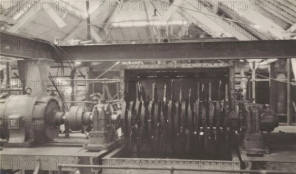 Canecutter, photograph, Electrically powered rotor of the canecutter at the Kaliwoengoe Sugar Factory west of Semarang. Part of the binder containing photographs of machines from NV Machinefabriek Braat in Surabaya intended for the Dutch sugar industry in Java, from the period 1917-1938., Java, 1917 - 1938, photographer, paper, gelatin silver print, gelatin silver print on photographic paper, height 155 mm x width 231 mm, Person, NV Machinefabriek Braat, colonial system, (non-fruit) products of plants or trees: sugarcane, factory-interior, machine shop, machines, parts of machines, tools and appliances, economic history, overseas history, sugar industry, business history, Period, A sepia-toned industrial interior showing large mechanical equipment arranged on a metal platform, including a cylindrical motor-like unit with a rounded housing on the left and a long shaft connected to a series of closely spaced disk-shaped components extending toward the right; overhead structural beams and...