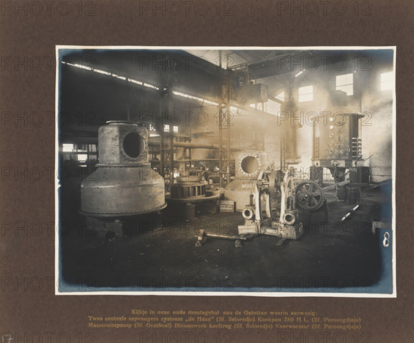 A glimpse into our old assembly hall on the Gatottan ..., album page, photograph, Album page with a photo of a factory hall containing various machines. Manufactured by Machinefabriek Braat and intended for the Seloredjo, Paroengdjaja, and Oemboel Sugar Factories, 1923. Part of the photo album Machinefabriek Braat Soerabaia-Djocja-Tegal, ca. 1916-1924., Surabaya, 1923, photographer, Java, East Java, paper, pasteboard, matte daylight collodion silver print, height 170 mm x width 231 mm, height 240 mm x width 290 mm, Person, NV Machinefabriek Braat, Oemboel Sugar Factory, Seloredjo Sugar Factory, Paroengdjaja Sugar Factory, colonial system, factory-interior, machine shop, machines, parts of machines, tools and appliances, economic history, overseas history, sugar industry, company history, Period, 1916 - 1924, The image shows the interior of an industrial workshop with large metal machinery and equipment arranged across the floor, including cylindrical tanks with round openings, a vertic...