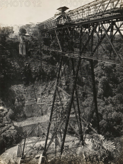Railway bridge over the Ci Somang under construction, album page, photograph, Album page with a photo of the railway bridge over the Ci Somang in Preanger under construction in 1931-1932. The three piers were supplied in 1931 by Machinefabriek Braat. Part of a photo album with photos of machines and structures of the NV Machinefabriek Braat in Surabaya, Sukabumi, and Tegal from the period 1931-1937., date: 'Tji Somang 26-11-'31', Preanger, 1931-11-16, photographer, Java, West-Java, paper, pasteboard, gelatin silver print, developed gelatin silver print, height 240 mm x width 179 mm, height 250 mm x width 320 mm, Other copies of the photos of the construction of this bridge in album NG-2002-84-C., Person, NV Machinefabriek Braat, railway, tramway, rack railway, bridge, economic history, overseas history, bridge building, company history, Ci Somang, Period, 1931 - 1937, A black-and-white photograph showing a large metal truss bridge spanning a deep rocky gorge, with tall lattice steel su...