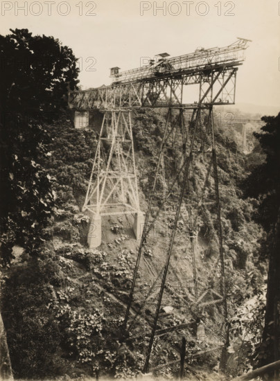 Railway bridge over the Ci Somang under construction, album page, photograph, Album page with a photo of the railway bridge over the Ci Somang in Preanger under construction in 1931-1932. The three piers were supplied in 1931 by Machinefabriek Braat. Part of a photo album with photos of machines and structures of the NV Machinefabriek Braat in Surabaya, Sukabumi, and Tegal from the period 1931-1937., date: '16-1-'32', Preanger, 1932-01-16, photographer, Java, West-Java, paper, pasteboard, gelatin silver print, developed gelatin silver print, height 240 mm x width 179 mm, height 250 mm x width 320 mm, Other copies of the photos of the construction of this bridge in album NG-2002-84-C., Person, NV Machinefabriek Braat, railway, tramway, rack railway, bridge, economic history, overseas history, bridge building, company history, Ci Somang, Period, 1931 - 1937, A large steel trestle bridge spans a deep, tree-covered ravine, supported by tall lattice towers with concrete footings; the bridge...