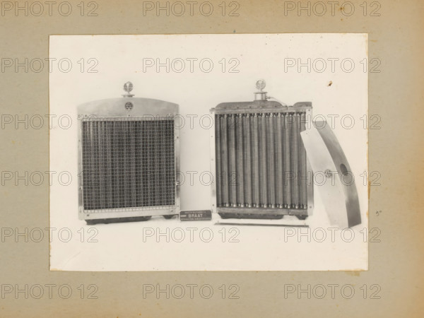 Radiator for roller, album page, photograph, Album page with a photo of the front and back of a radiator for a roller. Part of a photo album with photos of machines and constructions of the NV Machinefabriek Braat in Surabaya, Sukabumi and Tegal from the period 1931-1937., Java, 1931 - 1937, photographer, paper, pasteboard, gelatin silver print, developing gelatin silver print, height 166 mm x width 222 mm, height 250 mm x width 320 mm, Person, NV Machinefabriek Braat, machines, parts of machines, tools and appliances, economic history, overseas history, company history, Period, A photograph mounted on a beige backing shows two metal radiators displayed side by side on a white background with a curved metal panel leaning against the right radiator; each radiator has a circular ornament on top, fine vertical cooling fins, and a rectangular frame, and a small rectangular plaque sits below the radiators on the surface.