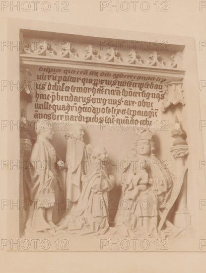 Bas-relief in the St. Hippolytus Church in Middelstum, photograph, annotation: 'Bas-relief in the Dutch Reformed Church in Middelstum', annotation: 'Middelstum', St. Hippolytus Church, 1890 - 1910, photographer, Middelstum, Attributed to, paper, pasteboard, albumen print, height 223 mm x width 171 mm, sculpture (relief, sculpture), A carved stone relief framed by a rectangular border shows a group of robed figures arranged in a scene, with one seated figure wearing a crown and holding a small child on their lap, flanked by standing and kneeling figures in long draped garments; above them is a horizontal panel with ornate floral trim and rows of stylized script carved into the stone, and decorative architectural elements appear at the top corners and sides.