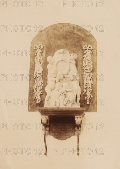 Tomb monument of Jacob van Campen in the St. George's Church in Amersfoort, photograph, annotation: 'Amersfoort', annotation: 'Amersfoort, S. Joriskerk, ... in memory of Jacob van Kampen obiit 1657', St. George's Church (Amersfoort), 1891, photographer, Amersfoort, Attributed to, paper, pasteboard, albumen print, height 222 mm x width 164 mm, Person, Jacob van Campen, other memorial structures, A carved stone relief mounted on a wall with an arched dark backdrop shows a group of cherubic figures clustered around a central oval cartouche, with some figures sitting and others standing; one figure holds a small skull near the center. Flanking the relief on both sides are vertical decorative garlands tied with bows at the top, each garland incorporating ribbonlike elements and ornamental shapes. The relief rests on a projecting stone shelf supported by carved brackets, with two curved metal supports hanging down from the shelf. The overall image has a sepia tone and shows the wall surround...