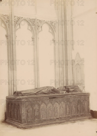 Tomb monument of Gwijde van Avesnes in the Cathedral of Utrecht, photograph, annotation: 'Utrecht', annotation: 'Cathedral in Utrecht, tomb of Bishop Guy van Avesnes, Sept 1891', Cathedral of Utrecht, 1891, photographer, Utrecht, Attributed to, paper, pasteboard, albumen print, height 240 mm x width 171 mm, Person, Gwijde van Avesnes, interior of church, grave-building, monumental tomb, A stone tomb with a rectangular base and carved arched panels along its sides occupies the foreground, topped by two recumbent effigies draped in robes. Behind the tomb rise tall, slender columns and pointed arch openings with ornate tracery in the spandrels, and a section of a wall with a recessed arched niche is visible to the right. The scene is rendered in muted monochrome tones with soft lighting and subtle shadows.