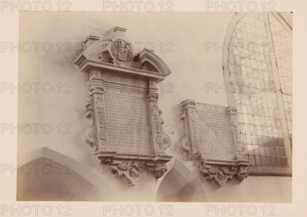 Grave monument in the Cathedral of Utrecht, photograph, annotation: 'Cathedral in Utrecht, Sept 1891', annotation: 'Utrecht', Cathedral of Utrecht, 1891, photographer, Utrecht, Attributed to, paper, pasteboard, albumen print, height 166 mm x width 240 mm, interior of church, grave-building, monumental tomb, A sepia-toned photograph showing two ornate stone memorial plaques mounted on a wall, each with carved decorative borders and scroll-like brackets at the bottom featuring skull motifs, with a large arched multi-pane window to the right composed of rectangular panes and leading strips, and smooth plastered wall surfaces surrounding the plaques.