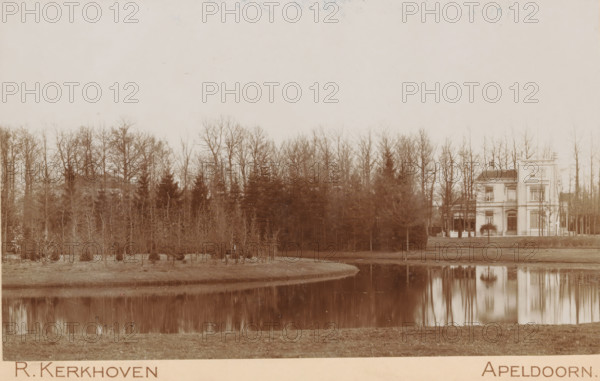 Oranjepark, Oranjepark in Apeldoorn, cabinet photograph, stamp: 'AF van Wieringen, Boek-, Muziek-, & Kunsthandel, Apeldoorn', collector's mark: 'Vosmaer', photographer: Richard Kerkhoven, Apeldoorn, vendor: AF van Wieringen, 1893 - 1902, Richard Kerkhoven, AF van Wieringen, photographer, vendor, paper, pasteboard, baryta paper, daylight collodion silver print, height 108 mm x width 168 mm, park, A calm body of water reflects a line of bare trees and a light-colored multi-story house with a tower-like section near the right edge of the scene; the house has prominent windows, a doorway, and an adjacent covered porch area, while the foreground shows a grassy bank and the water's edge, and the background is filled with tall leafless trees forming a continuous treeline across the image.